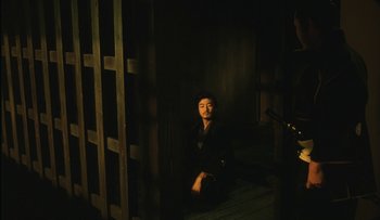 Movie still from “Taboo” (1999), directed by Nagisa Ôshima – A man sitting in a dark room with a sword; Wide shot, High angle