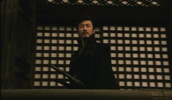 Movie still from “Taboo” (1999), directed by Nagisa Ôshima – A man holding a katana in front of a wall; Medium shot, Low angle