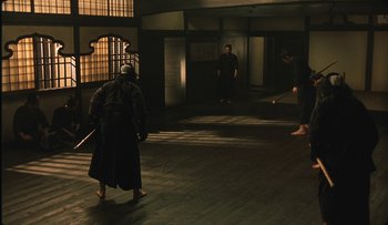 Movie still from “Taboo” (1999), directed by Nagisa Ôshima – A man in a black robe is holding a sword in a dark room; Wide shot, High angle
