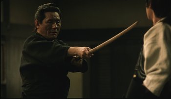 Movie still from “Taboo” (1999), directed by Nagisa Ôshima – A man holding a wooden stick in his hands; Close Up shot, Over the shoulder angle