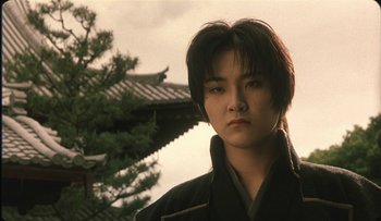 Movie still from “Taboo” (1999), directed by Nagisa Ôshima – A young man in traditional japanese garb in front of an oriental building; Close Up shot, Low angle