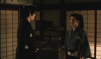 Movie still from “Taboo” (1999), directed by Nagisa Ôshima – Two men in black and white kimono standing next to each other in a room; Medium shot, Over the shoulder angle