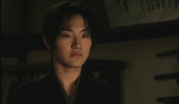 Movie still from “Taboo” (1999), directed by Nagisa Ôshima – A young asian man in a black shirt and black jacket; Close Up shot, Low angle