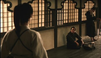 Movie still from “Taboo” (1999), directed by Nagisa Ôshima – Two men sitting on the ground in front of a window; Wide shot, Over the shoulder angle