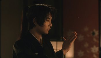 Movie still from “Taboo” (1999), directed by Nagisa Ôshima – A young man in a black kimono is holding his hands up; Close Up shot, Low angle