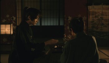 Movie still from “Taboo” (1999), directed by Nagisa Ôshima – Two people sitting at a table in front of a window; Medium shot, Over the shoulder angle