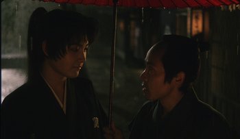 Movie still from “Taboo” (1999), directed by Nagisa Ôshima – Two men are talking under an umbrella in the dark; Close Up shot, Over the shoulder angle