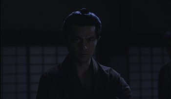 Movie still from “Taboo” (1999), directed by Nagisa Ôshima – A man in a black shirt is in the dark; Close Up shot, Low angle