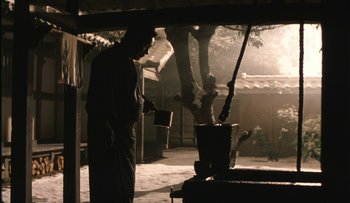 Movie still from “Taboo” (1999), directed by Nagisa Ôshima – A man standing in front of an outdoor stove holding a cup; Wide shot, Low angle
