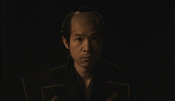 Movie still from “Taboo” (1999), directed by Nagisa Ôshima – A man in a black shirt and a black jacket; Close Up shot, Low angle