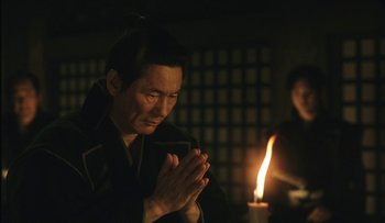 Movie still from “Taboo” (1999), directed by Nagisa Ôshima – A man praying in front of a lit candle; Medium shot, Low angle