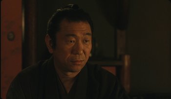Movie still from “Taboo” (1999), directed by Nagisa Ôshima – A man wearing a black robe and a black hat; Close Up shot, Over the shoulder angle