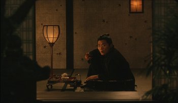 Movie still from “Taboo” (1999), directed by Nagisa Ôshima – A person sitting on a chair in a room; Medium shot, High angle
