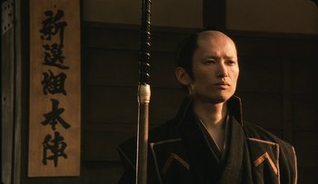Movie still from “Taboo” (1999), directed by Nagisa Ôshima – A man in a black robe holding a sword; Close Up shot, Low angle