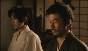 Movie still from “Taboo” (1999), directed by Nagisa Ôshima – Two men in traditional japanese garb looking at the camera; Close Up shot, Over the shoulder angle