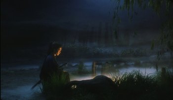 Movie still from “Taboo” (1999), directed by Nagisa Ôshima – A woman sitting on the ground in front of a body of water at night; Wide shot, Low angle