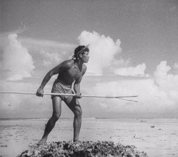 Movie still from “Tabu: A Story of the South Seas” (1931), directed by F.W. Murnau – A man holding a spear while standing on a beach; Wide shot, Low angle