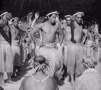 Movie still from “Tabu: A Story of the South Seas” (1931), directed by F.W. Murnau – A black and white photo of a group of men in grass skirts; Medium shot, High angle