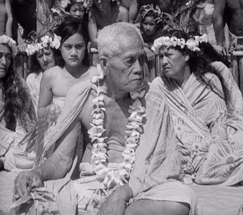 Movie still from “Tabu: A Story of the South Seas” (1931), directed by F.W. Murnau – An older man sitting next to a group of people; Medium shot, High angle