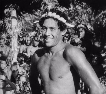 Movie still from “Tabu: A Story of the South Seas” (1931), directed by F.W. Murnau – A man with a wreath on his head is standing in front of a group of people; Close Up shot, Low angle