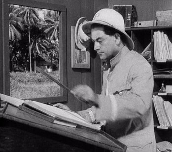 Movie still from “Tabu: A Story of the South Seas” (1931), directed by F.W. Murnau – A man wearing a white hat is working at a desk; Medium shot, High angle