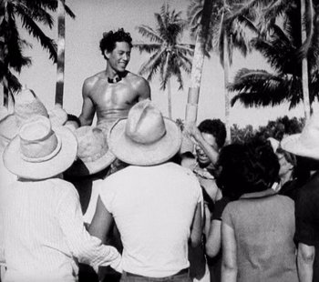Movie still from “Tabu: A Story of the South Seas” (1931), directed by F.W. Murnau – A man is holding a drum in a crowd of people; Medium shot, High angle