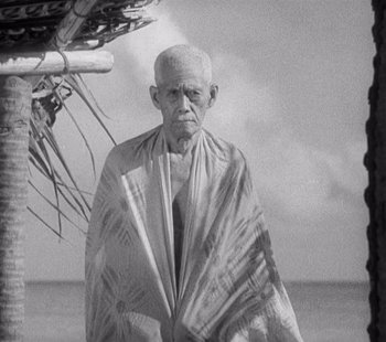 Movie still from “Tabu: A Story of the South Seas” (1931), directed by F.W. Murnau – An old man standing under an umbrella on the beach; Medium shot, Low angle