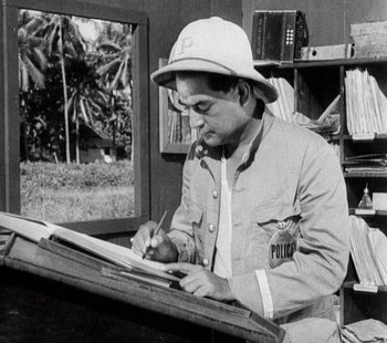 Movie still from “Tabu: A Story of the South Seas” (1931), directed by F.W. Murnau – A man sitting at a desk writing on a piece of paper; Medium shot, High angle