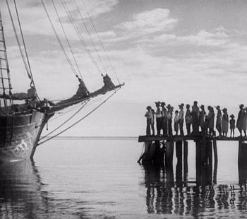 Movie still from “Tabu: A Story of the South Seas” (1931), directed by F.W. Murnau – A group of people standing on a pier next to a boat; Extreme Wide shot, Low angle