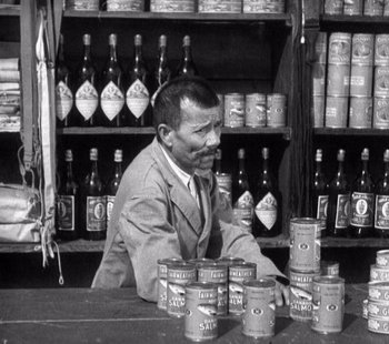 Movie still from “Tabu: A Story of the South Seas” (1931), directed by F.W. Murnau – A man sitting at a counter in front of cans of food; Medium shot, Over the shoulder angle