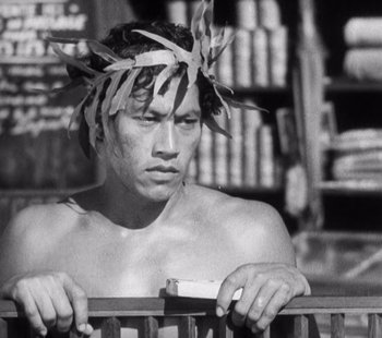 Movie still from “Tabu: A Story of the South Seas” (1931), directed by F.W. Murnau – A shirtless man with a feather wreath on his head looking at the camera; Close Up shot, Low angle