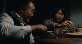 Movie still from “Taipei Story” (1985), directed by Edward Yang – Two men sitting at a table with a glass of whiskey; Medium shot, Over the shoulder angle