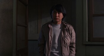 Movie still from “Taipei Story” (1985), directed by Edward Yang – A man standing in the dark wearing a tan jacket; Medium shot, Over the shoulder angle