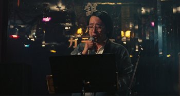 Movie still from “Taipei Story” (1985), directed by Edward Yang – A man in glasses is singing in front of a microphone; Medium shot, Low angle