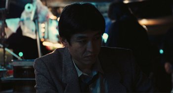 Movie still from “Taipei Story” (1985), directed by Edward Yang – A man in a suit and tie sitting down; Close Up shot, Over the shoulder angle
