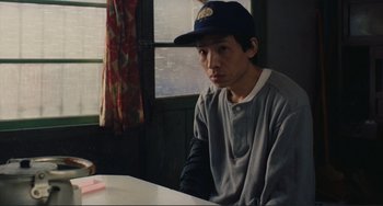 Movie still from “Taipei Story” (1985), directed by Edward Yang – A man sitting at a table wearing a hat; Medium shot, High angle