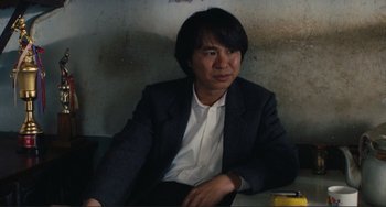 Movie still from “Taipei Story” (1985), directed by Edward Yang – A man in a suit sitting on a table; Medium shot, High angle