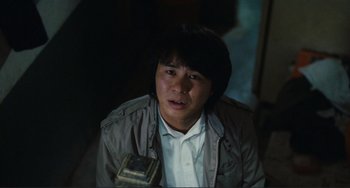 Movie still from “Taipei Story” (1985), directed by Edward Yang – A man in a brown jacket is sitting in a dark room; Close Up shot, Low angle
