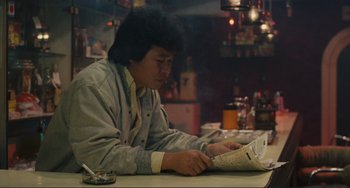 Movie still from “Taipei Story” (1985), directed by Edward Yang – A man sitting at a table reading a newspaper; Medium shot, Low angle