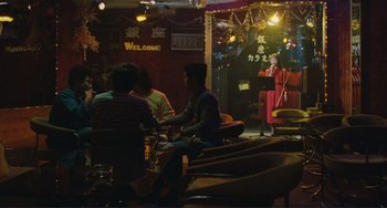 Movie still from “Taipei Story” (1985), directed by Edward Yang – A group of people sitting in a room with a microphone; Wide shot, Over the shoulder angle