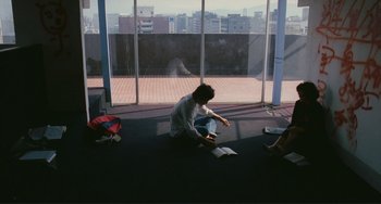 Movie still from “Taipei Story” (1985), directed by Edward Yang – A man sitting on the ground reading a book; Wide shot, High angle