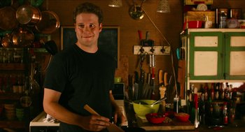 Movie still from “Take This Waltz” (2011), directed by Sarah Polley – A man standing in front of a counter holding a knife; Medium shot, Over the shoulder angle
