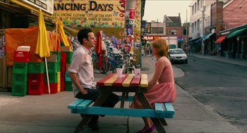Movie still from “Take This Waltz” (2011), directed by Sarah Polley – A man and a woman sitting at a picnic table on the sidewalk; Wide shot, Over the shoulder angle