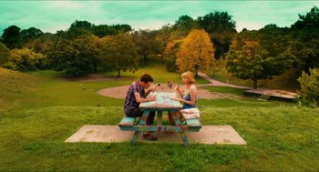 A man and a woman sitting at a picnic table in a park