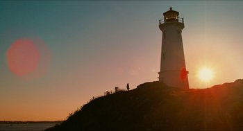A person standing on top of a hill next to a light house