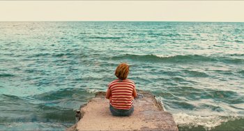 Movie still from “Take This Waltz” (2011), directed by Sarah Polley – A person sitting on a rock near the ocean; Wide shot, High angle