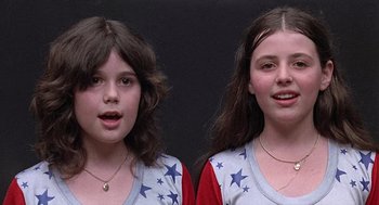 Movie still from “Taking Off” (1971), directed by Milos Forman – Two young girls posing for a picture in front of a black background; Close Up shot, Overhead angle