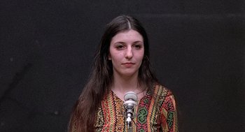 Movie still from “Taking Off” (1971), directed by Milos Forman – A woman standing in front of a microphone with long hair; Close Up shot, High angle