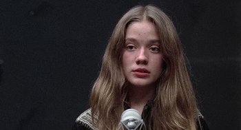 Movie still from “Taking Off” (1971), directed by Milos Forman – A young woman with long hair is standing in front of a microphone; Close Up shot, Low angle
