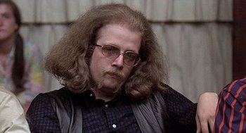 Movie still from “Taking Off” (1971), directed by Milos Forman – A man with long hair wearing glasses and a black shirt; Close Up shot, Low angle